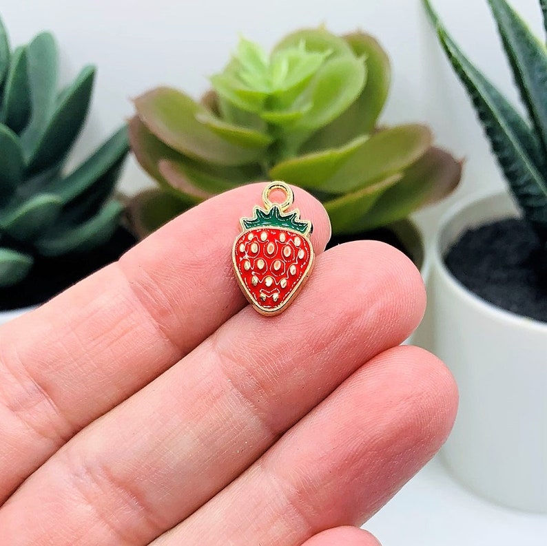 Puede incluir: Encanto de tono dorado con una fresa de esmalte rojo y verde con un bucle para sujetar a joyas o manualidades.