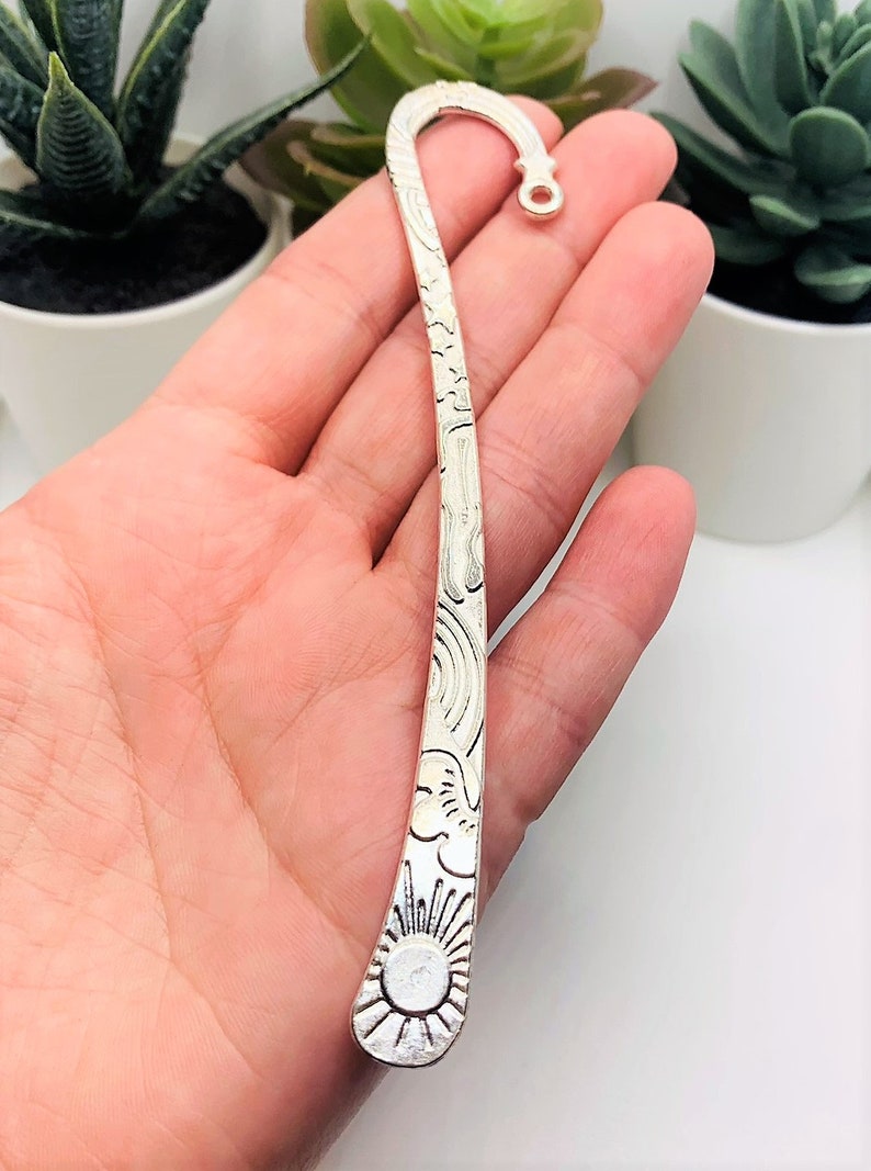 May include: Silver bookmark with a sun and clouds design. The bookmark is curved and has a small loop at the top.