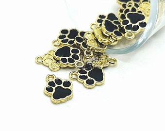 May include: A pile of gold-colored metal paw print charms with black enamel. The charms are spilling out of a glass jar.