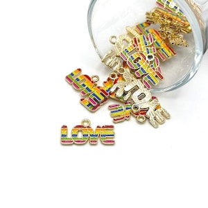 May include: A close-up of a group of gold-colored metal charms with a rainbow stripe design. The charms spell out the word "LOVE".