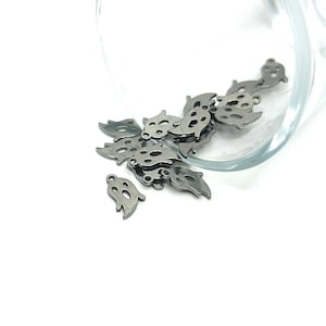 May include: A pile of silver metal ghost charms with a hole for stringing. The charms are in a glass bowl on a white background.