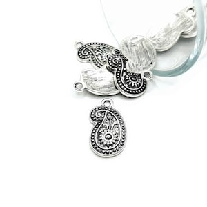 May include: Silver-toned metal charms in the shape of paisley designs. The charms have a black oxidized finish and intricate details.