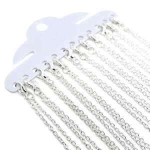 May include: A pack of 12 silver chains, each with a lobster clasp, displayed on a white card.