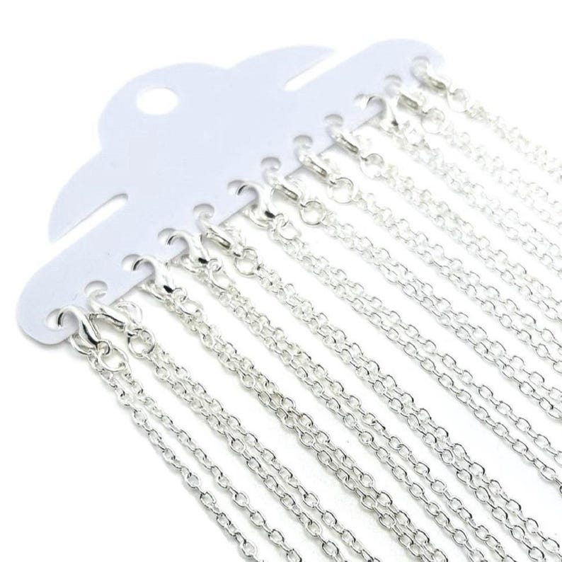 May include: A pack of 12 silver chains, each with a lobster clasp, displayed on a white card.