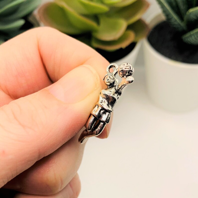May include: Silver charm of a basketball player in mid-air, holding a basketball. The charm is detailed and has a realistic design.