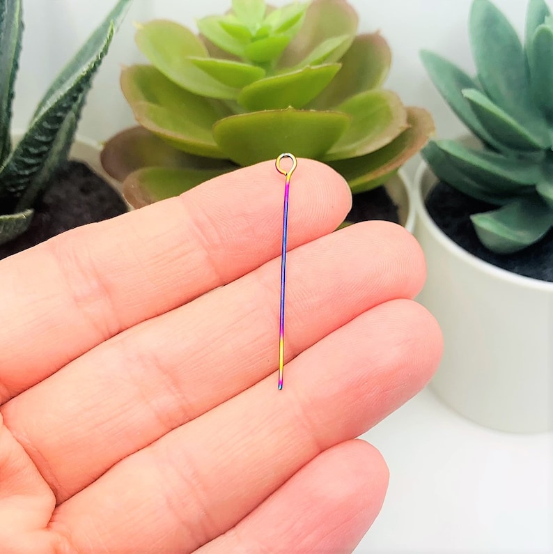 May include: A rainbow coloured metal head pin with a gold loop at the top. The pin is approximately 2.5 cm long.