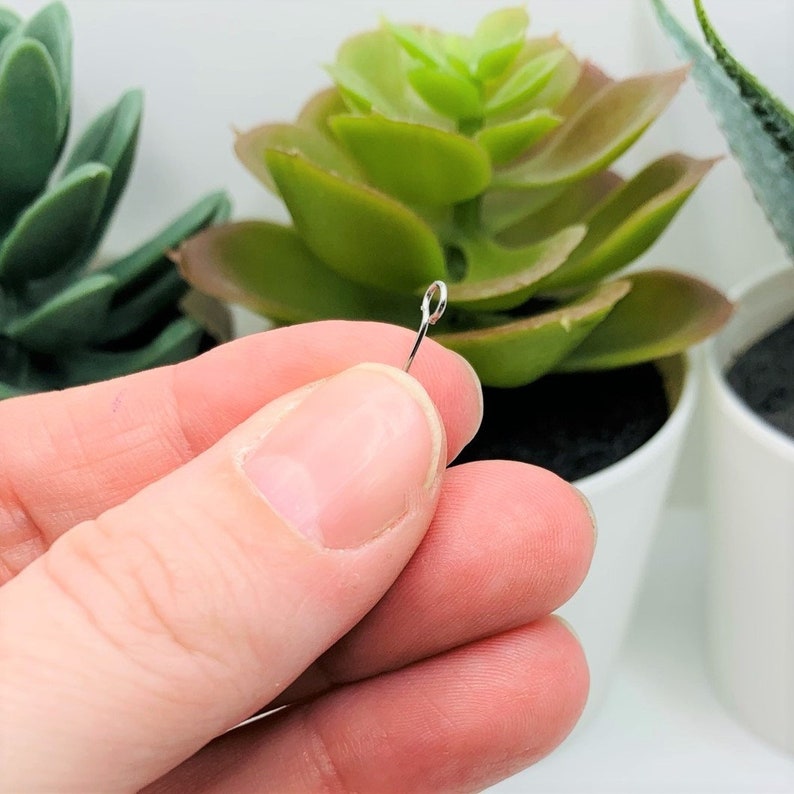 May include: A close-up of a silver wire loop with a small loop at the end. The wire is held between two fingers.