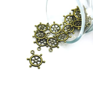 May include: A close-up of a glass jar filled with antique gold-toned metal ship wheel charms. The charms are spilling out of the jar onto a white surface.