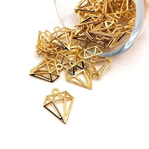 May include: A large pile of gold-colored metal diamond-shaped charms with a hole at the top for hanging. The charms are arranged in a bowl and some are spilling out.