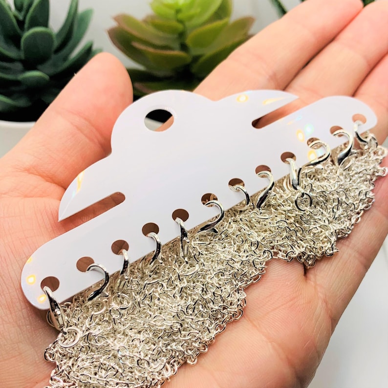 May include: A white plastic card with multiple silver chains attached. The chains are arranged in a cascading pattern and are ready to be used for jewellery making.