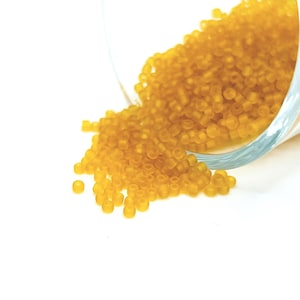 May include: A glass jar filled with small, opaque, yellow beads. The jar is tipped over, spilling the beads onto a white surface.
