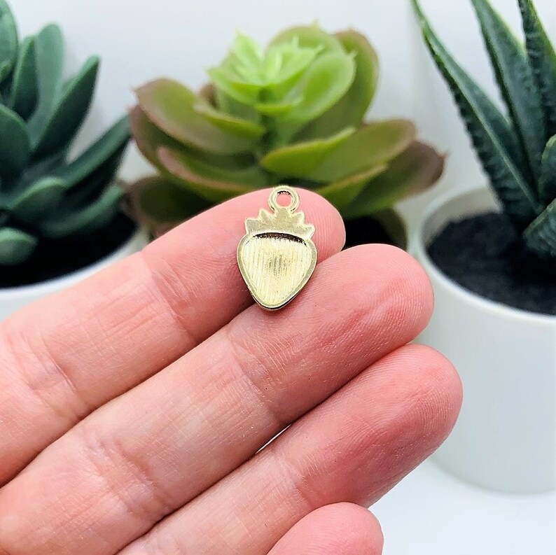 Puede incluir: Encanto de fresa de metal dorado con superficie texturizada. El encanto tiene un bucle en la parte superior para sujetarlo a joyas u otras manualidades.