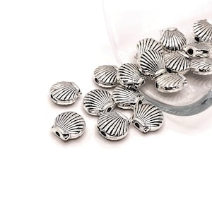 May include: Silver metal seashell charms with a detailed design. The charms have a hole for stringing or attaching to jewelry.