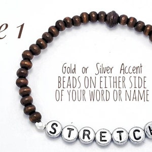 以下が含まれることがあります： 茶色の木製ビーズブレスレット。シルバーのアクセントビーズが「STRETCH」という単語の両側にあり、シルバーの文字ビーズで綴られています。このブレスレットはストレッチブレスレットなので、留め金がありません。