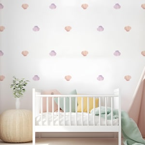 May include: A white cot with a white mattress and a green and yellow patterned blanket. The wall behind the cot is white with a pattern of pink and orange seashells.