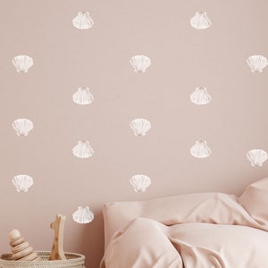May include: A light pink wall with a repeating pattern of white seashells. The wall is behind a bed with a white and pink duvet.