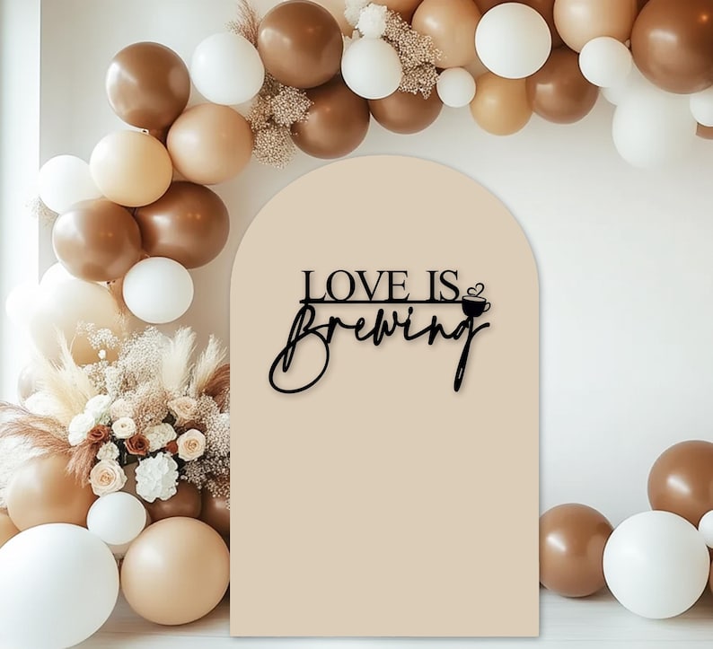 May include: A beige arch with the text "LOVE IS BREWING" in black with a small coffee cup icon. The arch is decorated with a garland of brown and white balloons.