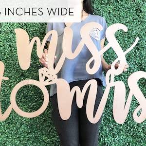 May include: A wooden sign with the words "miss to mrs" in cursive script. The sign is 36 inches wide and features a ring with a diamond in the center.