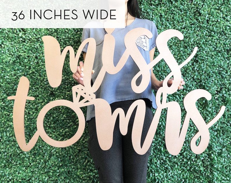 May include: A wooden sign with the words "miss to mrs" in cursive script. The sign is 36 inches wide and features a ring with a diamond in the center.