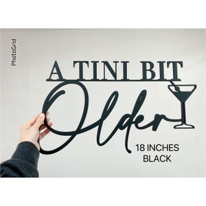May include: A black metal sign that reads "A TINI BIT Older" with a martini glass graphic. The sign is 18 inches long.