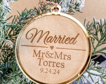 Może przedstawiać: Okrągła drewniana ozdoba ze złotą obwódką. Ozdoba jest wygrawerowana słowem "Married", imionami "Mr & Mrs Torres" i datą "9.24.24". Ozdoba jest otoczona gałązkami iglastymi.