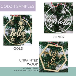 May include: A selection of personalized Christmas ornaments in gold, silver, and unpainted wood. The ornaments feature names like "Bella", "Charlotte", "Philip & Jen", and snowflake designs. The text "Color Samples" and "Unpainted Wood" are also visible.