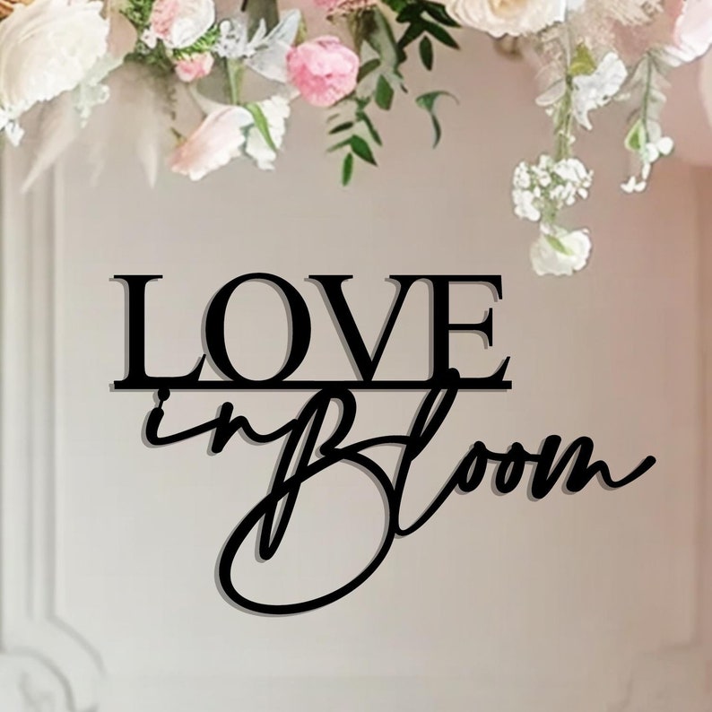 Op de afbeelding: Zwart metalen bord met de woorden "LOVE in BLOOM" in een decoratief lettertype.