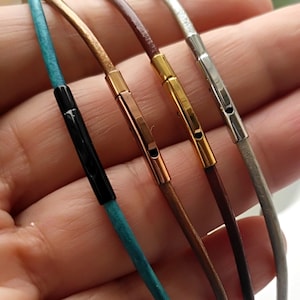 May include: Four leather cord necklaces with different coloured cords and metal clasps. The cords are turquoise, brown, gold, and grey.