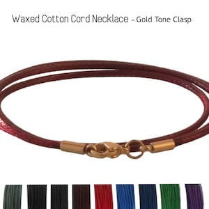 Peut inclure: Un collier en cordon de coton ciré de couleur bordeaux avec un fermoir doré. Le collier est présenté sur un fond blanc. L'image montre également une variété de couleurs pour le cordon, notamment le vert, le noir, le marron, le rouge, le bleu et le violet.
