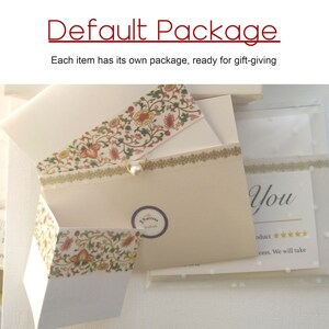 May include: A white gift box with a floral design and a pearl accent. The box is open and the inside is lined with white paper. The box is labeled "El Sastre" and has the text "You" on the side. The text "oduct" and five stars are also visible.