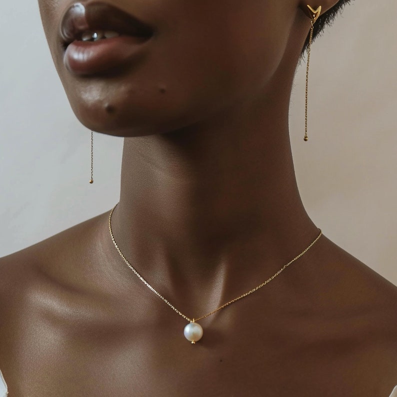 May include: A gold chain necklace with a single, large, white pearl pendant.