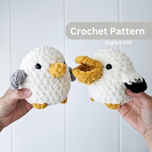 Może przedstawiać: Dwie pluszowe mewy amigurumi wykonane na szydełku, jedna z szarym skrzydłem, a druga z czarnym skrzydłem. Mewy są białe z żółtymi dziobami i czarnymi oczami. Wzór na szydełku jest dostępny w języku angielskim w formacie PDF.
