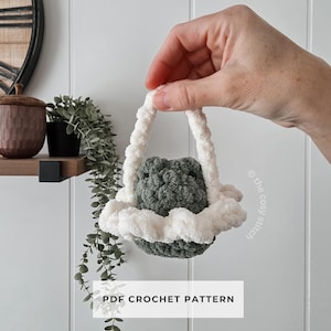 May include: A handmade crochet basket in shades of gray and white. The basket has a fluffy white trim and handle, and a gray interior. The text "PDF CROCHET PATTERN" is displayed on a white rectangle below the basket.