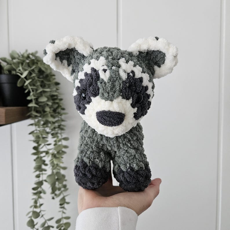 K&ouml;nnte beinhalten: Ein geh&auml;keltes Waschb&auml;r-Pl&uuml;schtier mit grauem und wei&szlig;em Fell. Das Spielzeug hat schwarze Augen und eine schwarze Nase.