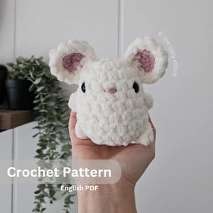 May include: Crochet pattern for a white amigurumi mouse with pink ears and black eyes. The pattern is available in English PDF format. "Crochet Pattern" and "English PDF" are written on the image.