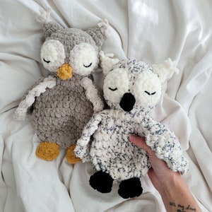 May include: Two crocheted owl plushies, one gray and one white with black speckles. The gray owl has yellow accents around the eyes and beak. The white owl has black eyes and a black beak.