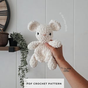 May include: A cream-colored plush toy shaped like a mouse, crafted from soft, chunky yarn with round ears, small black eyes, and a pink stitched nose. The text "the cosy stitch" and "PDF CROCHET PATTERN" are visible on the image.