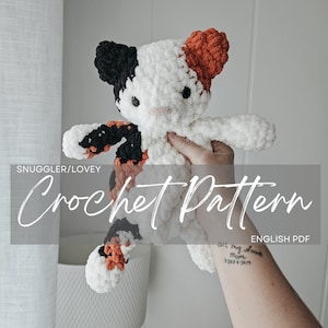 Puede incluir: Patrón de crochet para un juguete de peluche de gato calico. El juguete es blanco con manchas naranjas y negras. El patrón está disponible para descargar en PDF en inglés.