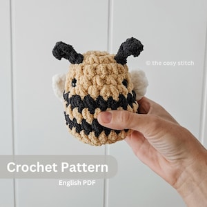 May include: Crochet pattern for a bee amigurumi toy. The bee is brown and black with white wings. The pattern is available in English PDF format.