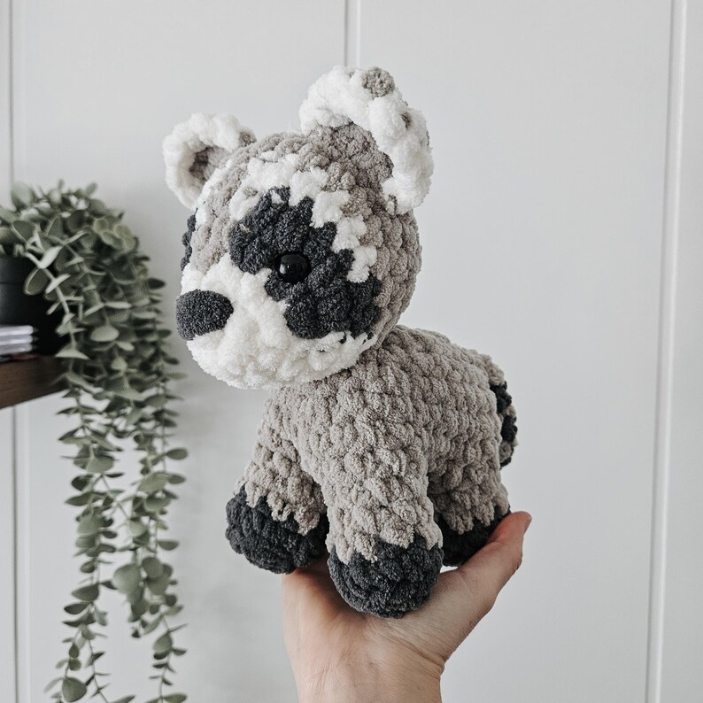 K&ouml;nnte beinhalten: Ein geh&auml;keltes Waschb&auml;r-Pl&uuml;schtier mit grauem und wei&szlig;em Fell. Das Spielzeug hat schwarze Augen und eine schwarze Nase.