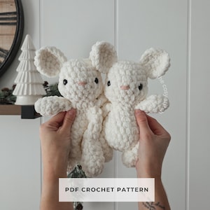 May include: Two white crochet bunny toys with black eyes and pink noses. The bunnies have large ears and are made of a soft, textured yarn. The text "PDF CROCHET PATTERN" is displayed on a white rectangle.