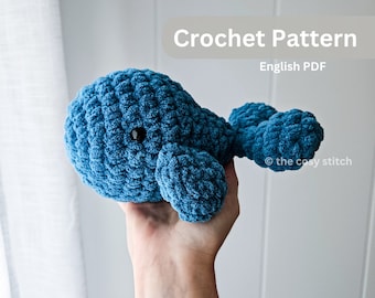 May include: A crocheted blue whale amigurumi toy with black eyes. The whale is being held in a hand. The image includes the text "Crochet Pattern English PDF @the cosystitch"