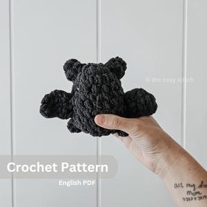May include: Crochet pattern for a black amigurumi octopus. The pattern is available as an English PDF download. The text "Crochet Pattern" and "English PDF" is visible in the image.