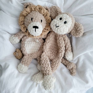 May include: Two crocheted stuffed animals, a lion and a monkey, are lying on a white bedspread. The lion is brown and white with a fluffy mane. The monkey is brown and white with a long tail.
