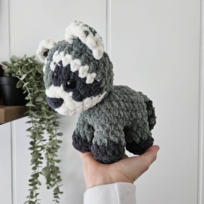 K&ouml;nnte beinhalten: Ein geh&auml;keltes Waschb&auml;r-Pl&uuml;schtier mit grauem und wei&szlig;em Fell. Das Spielzeug hat schwarze Augen und eine schwarze Nase.