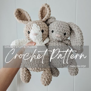 Peut inclure: Deux jouets en peluche de lapin en crochet de couleur beige et marron. Les lapins sont assis ensemble et ont des yeux noirs et des nez roses. Le texte "Chubby Stuffie/Plushie Crochet Pattern English PDF" est visible en bas de l'image.