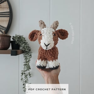 May include: A plush crochet goat toy made with brown and white fuzzy yarn, featuring small tan horns, dark eyes, and black stitched hooves. The text "the cosy stitch" and "PDF CROCHET PATTERN" are visible on the image, indicating a pattern design.