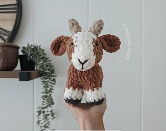 May include: A plush crochet goat toy made with brown and white fuzzy yarn, featuring small tan horns, dark eyes, and black stitched hooves. The text "the cosy stitch" and "PDF CROCHET PATTERN" are visible on the image, indicating a pattern design.