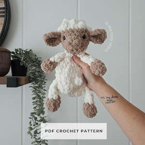 Könnte beinhalten: Ein handgefertigtes Häkellamm-Spielzeug in Weiß und Braun. Das Lamm hat einen flauschigen Körper, braune Ohren und ein braunes Gesicht. Der Text "PDF CROCHET PATTERN" wird unten im Bild angezeigt.