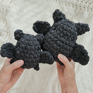 May include: Two plush crocheted black toys shaped like a small animal. The toys are made of a soft, fuzzy material and have a textured surface.